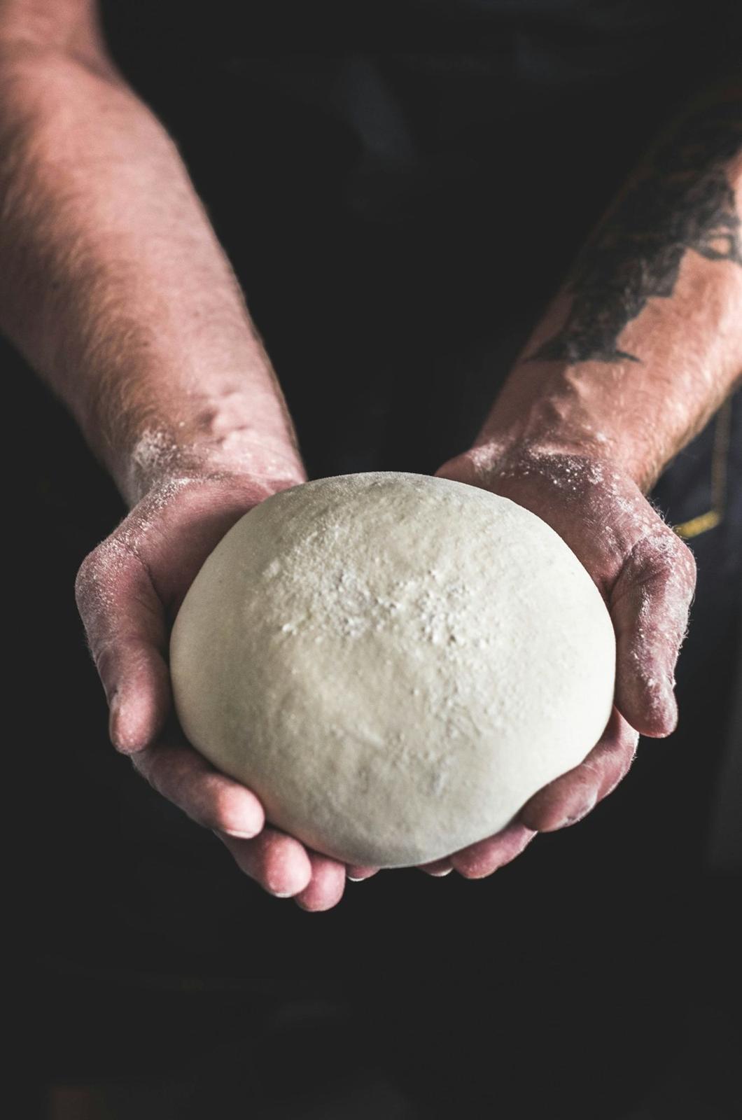 Mani del pizzaiolo che tengono il panetto d'impasto