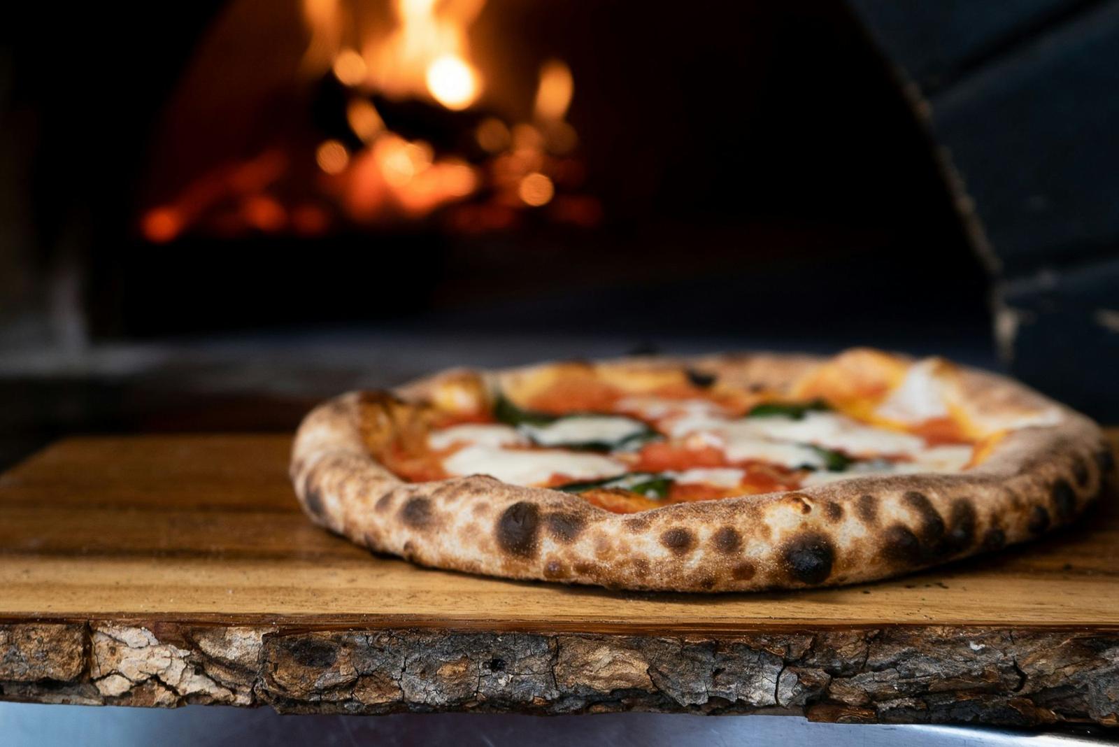 Pizza appena sfornata sul tagliere davanti al fuoco